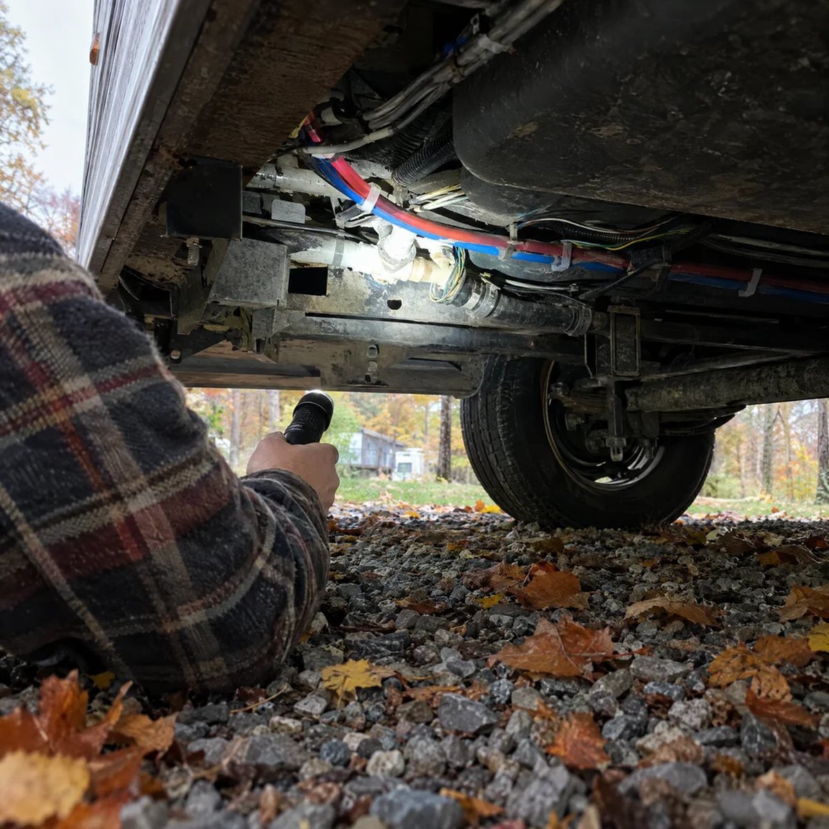 An RV owner, seen from behind, shining a flashlight under the skirt of a trailer