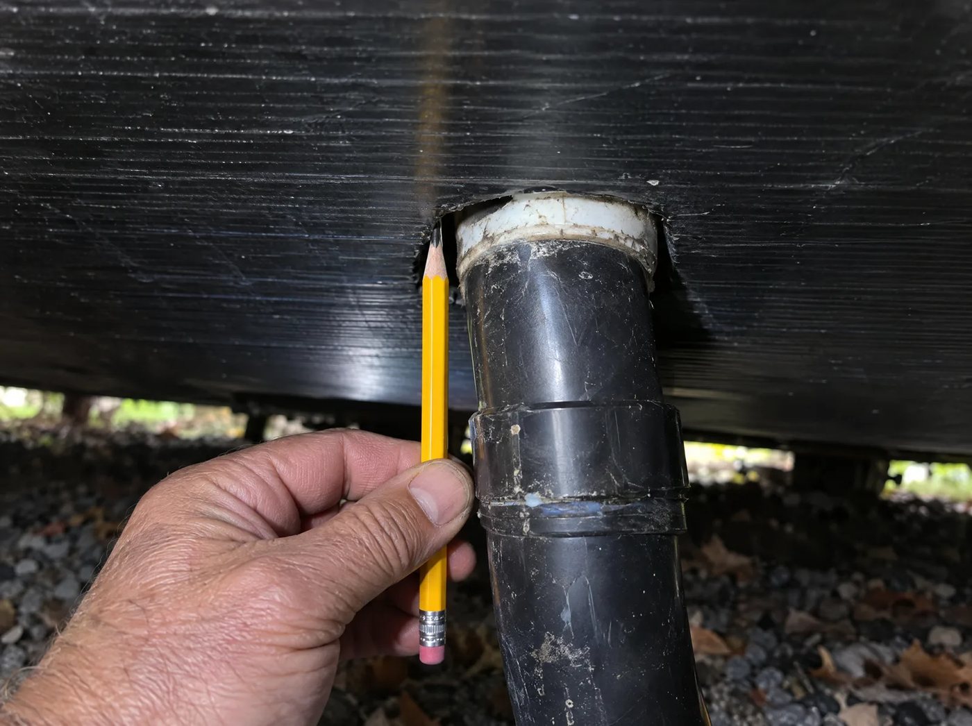 A hand holding a pencil next to a gap around the plumbing under a trailer