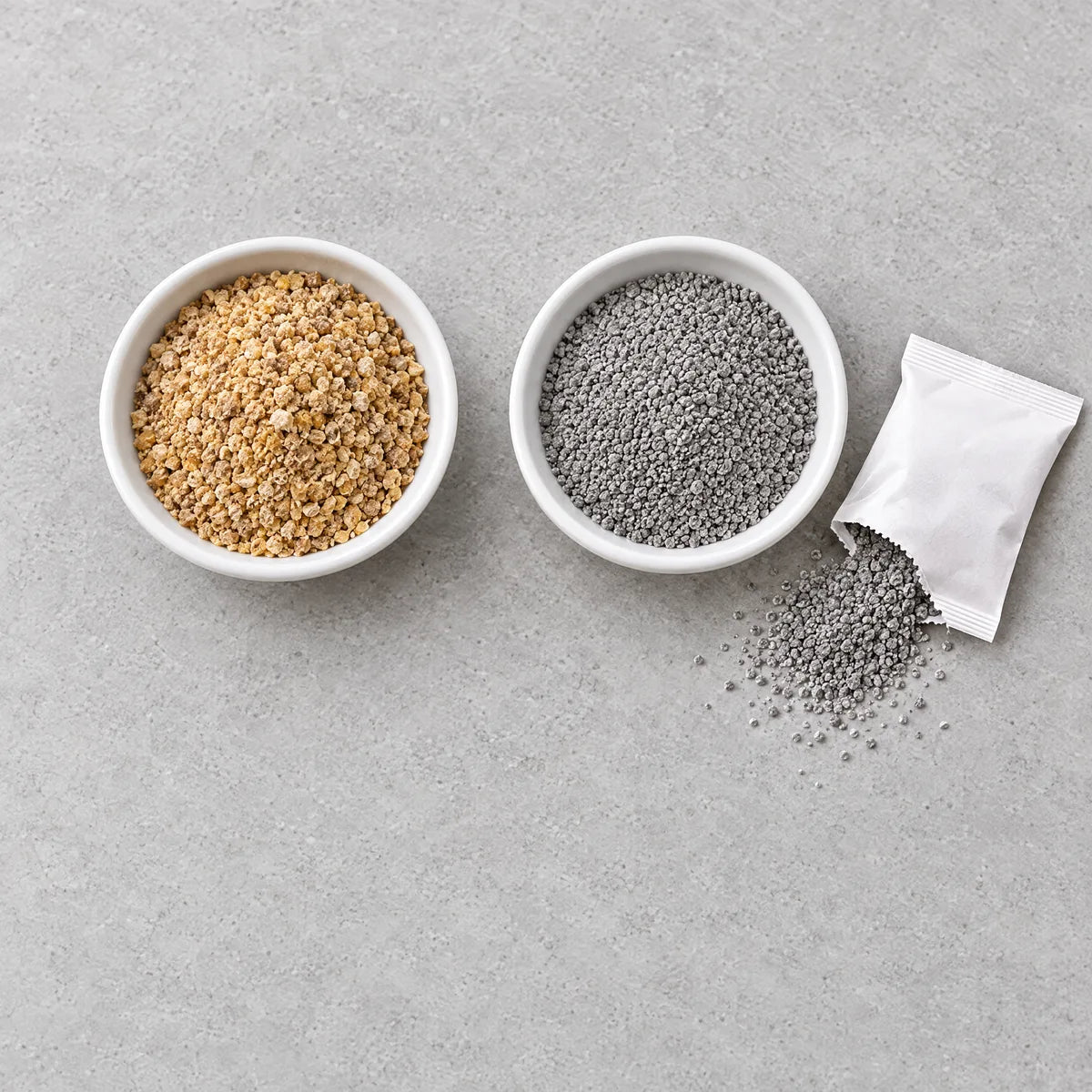 A dish of corn cob granules next to a dish of grey mineral fill from a cut-open pouch