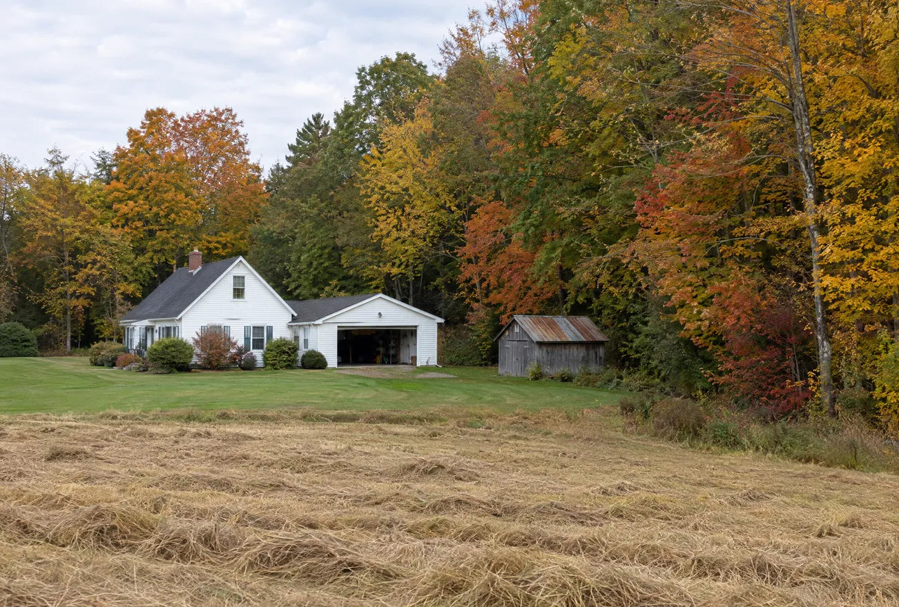 A farmhouse with a garage and shed, a field and woods right up to the yard